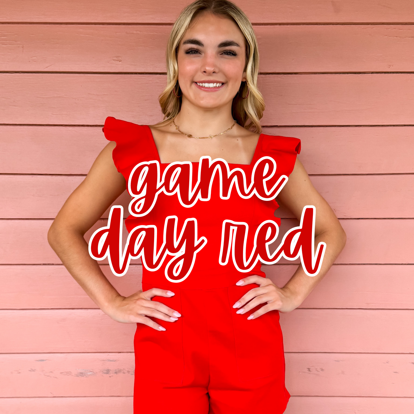 A smiling blonde woman poses against a pink wooden wall, wearing a bold red ruffled-sleeve jumpsuit. "Game Day Red" is overlaid in bold red script, showcasing a stylish outfit perfect for sporting events and team spirit.
