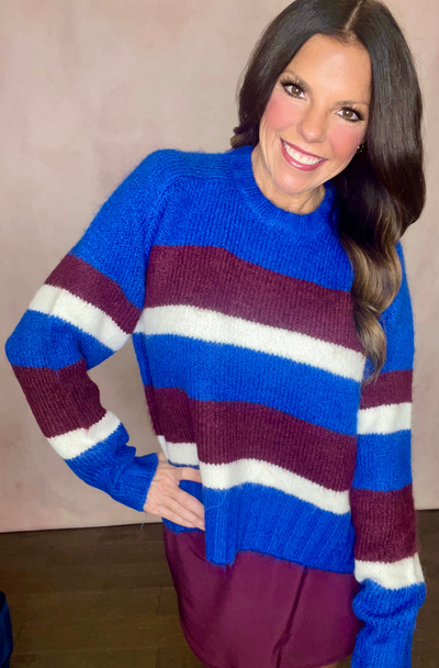 Woman wearing a blue, maroon, and white striped sweater against a plain background