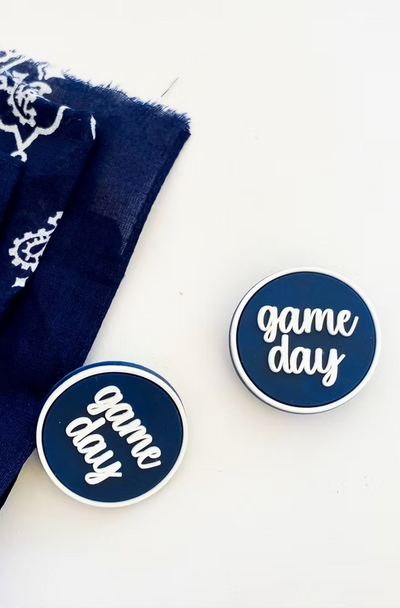 Pair of navy blue 'game day' boot buttons with white script lettering and border, styled beside matching bandana fabric.
