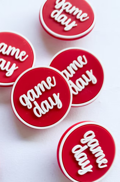 Stack of crimson 'game day' boot buttons with white script lettering and trim, perfect for college football fans and spirited gameday accessories.