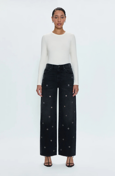 A person standing against a white background, wearing high-waisted black denim jeans with a relaxed fit and frayed hem, paired with a white top.