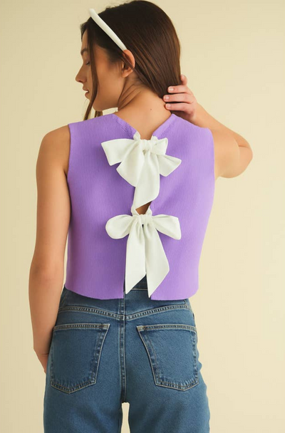Woman wearing a purple sleeveless top with white bows on the back against a beige background